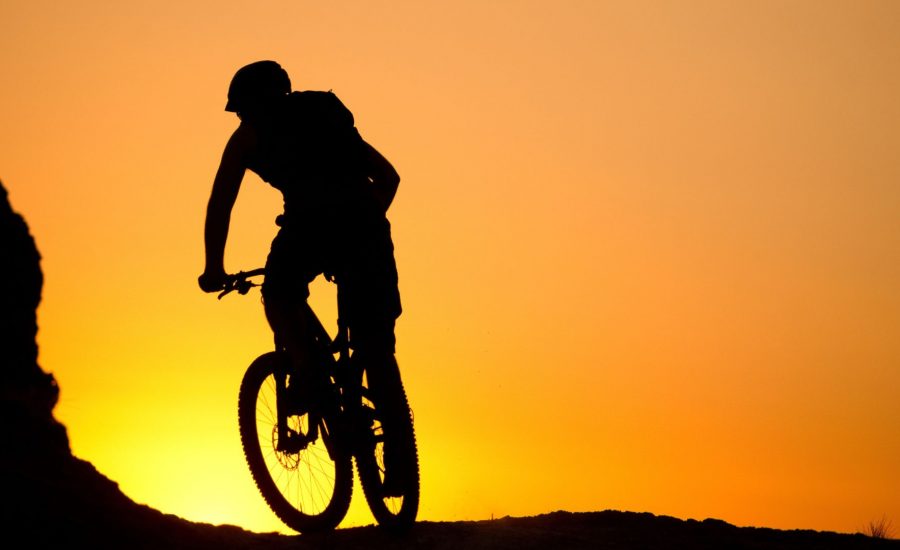 silhouette of man riding electric mountain bike at sunset