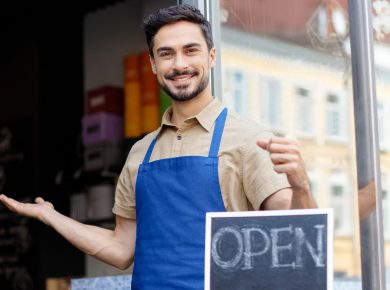 Man holding open sign outside cafe with open door