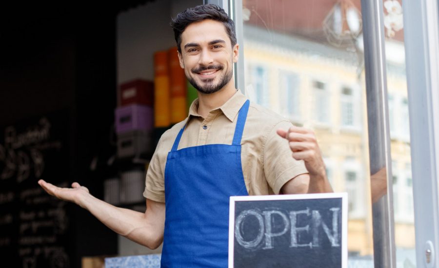 Man holding open sign outside cafe with open door