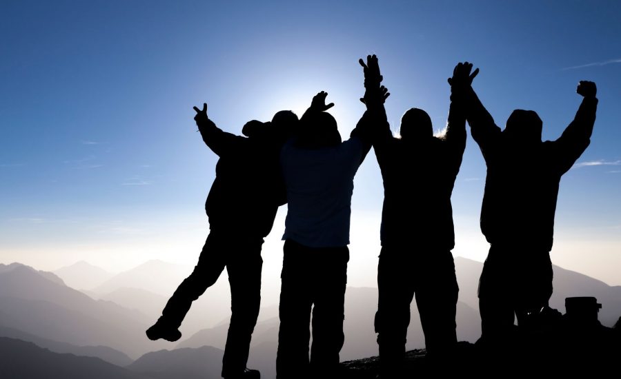silhouette group of climbers celebrating reaching the summit
